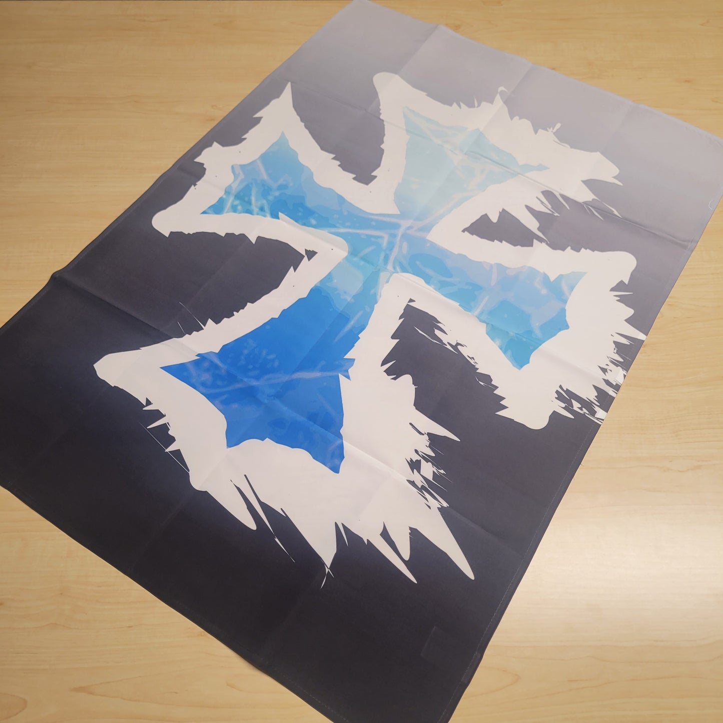 Dark themed tapestry featuring a jagged white frost cross symbol over a glowing icy blue center on a black background, laid flat on a wood surface.