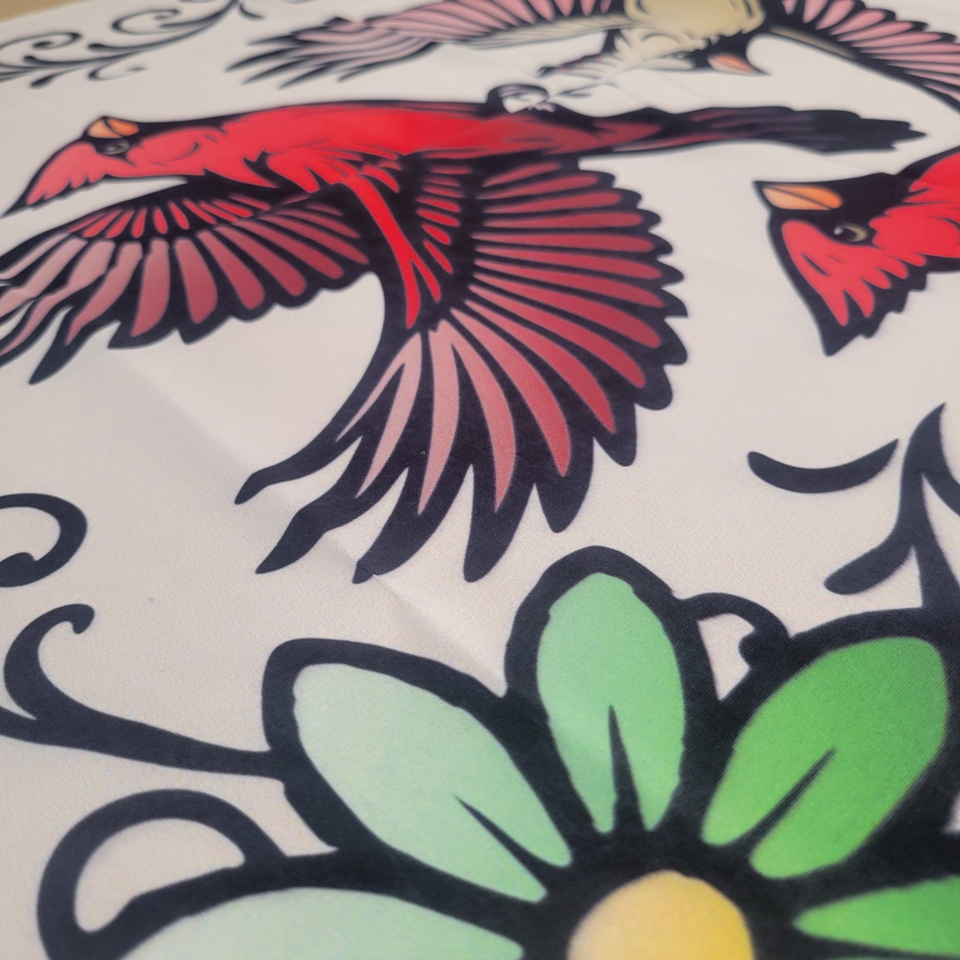 Close-up of bold tattoo-style red cardinals in flight over green floral designs and black illustrations on a beige fabric tapestry.