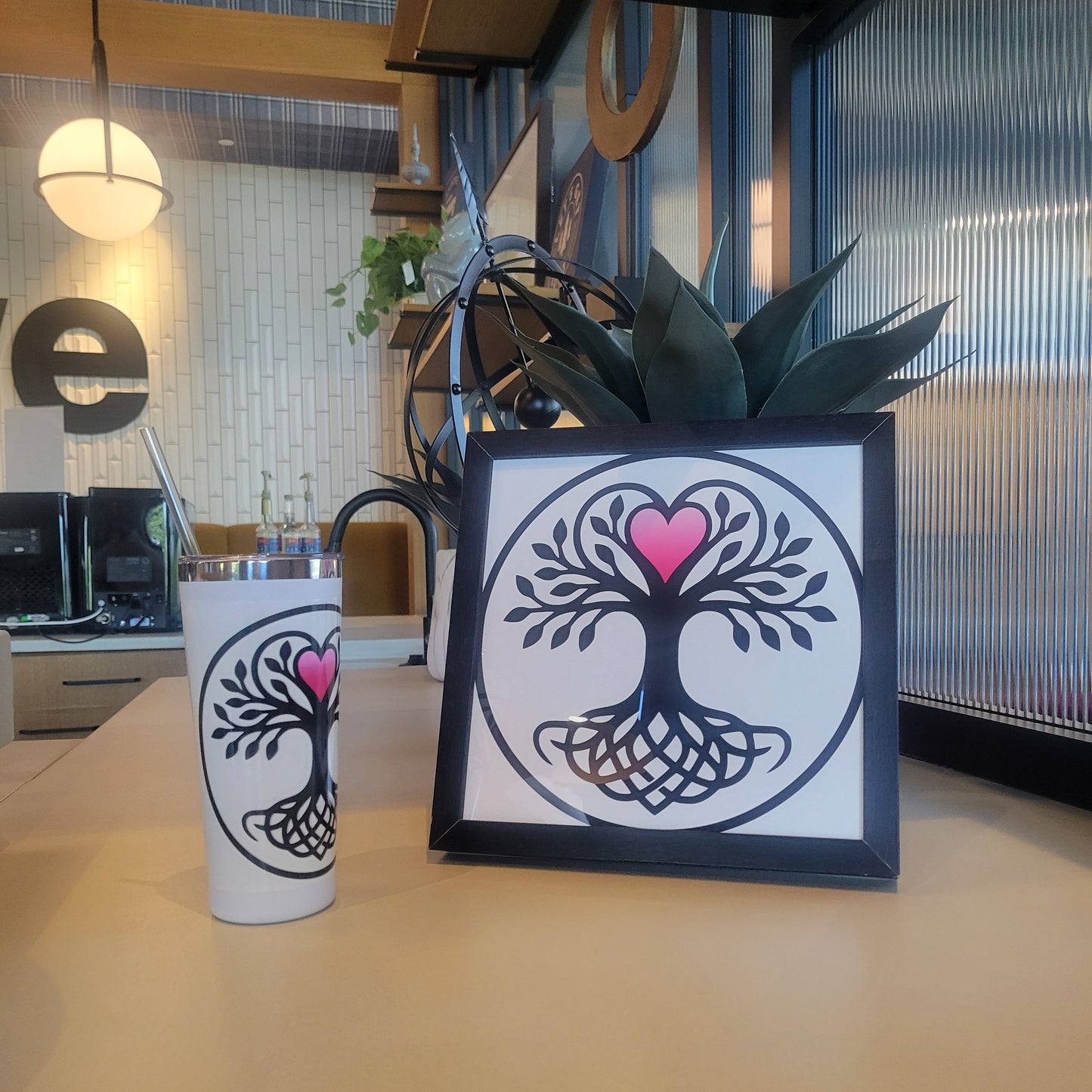 Black Norse tree of life with pink heart canopy in circular design, shown on white tumbler with straw and matching, black-framed wall art print.