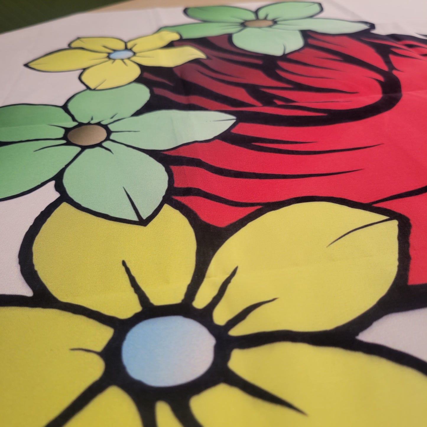 Close-up of bold line-art flowers in yellow and mint green with thick black outlines against swirling red cardinal feathers, printed on a tapestry.