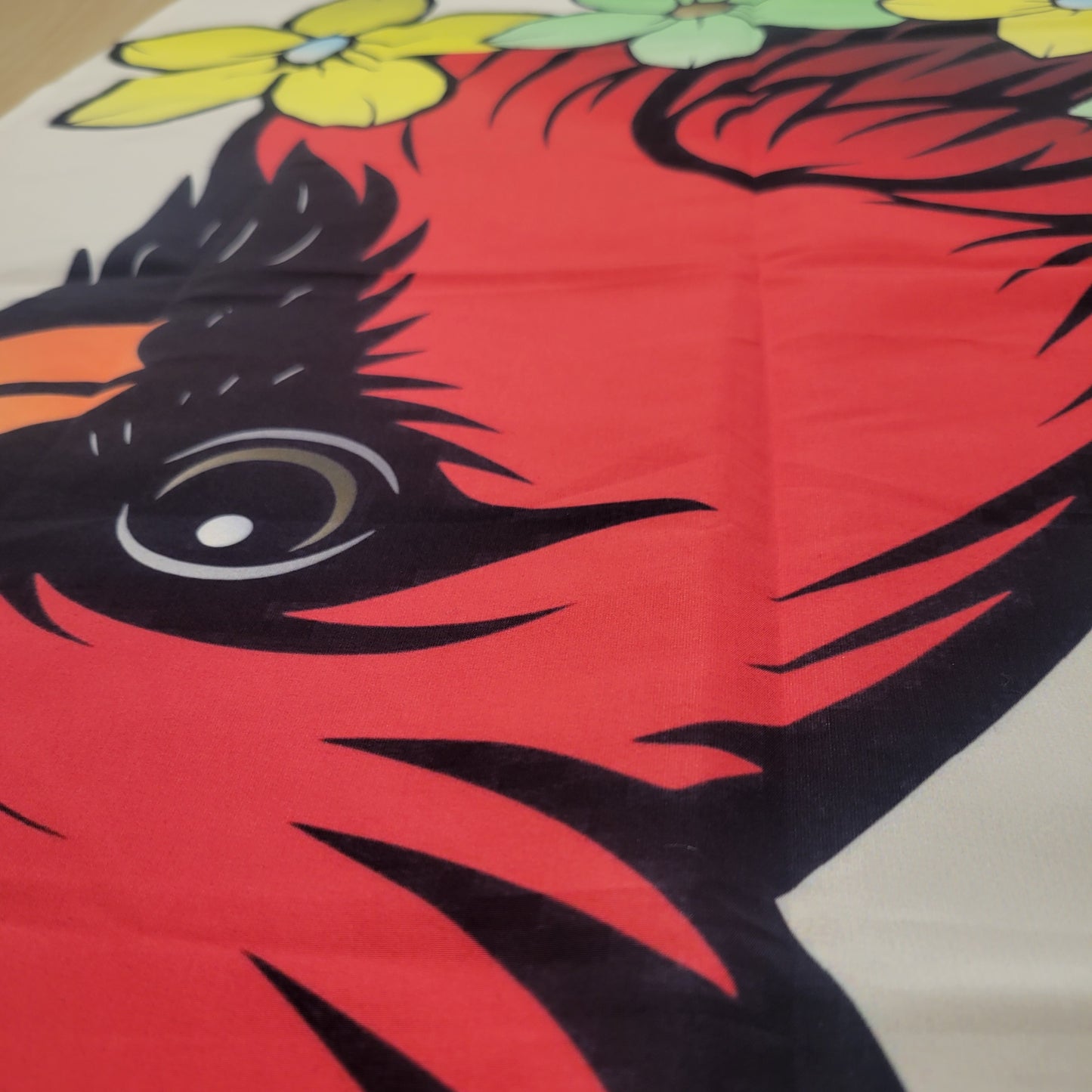Close-up of a bold illustrated red cardinal bird with a piercing eye and yellow and green flowers below, printed on a beige fabric tapestry.