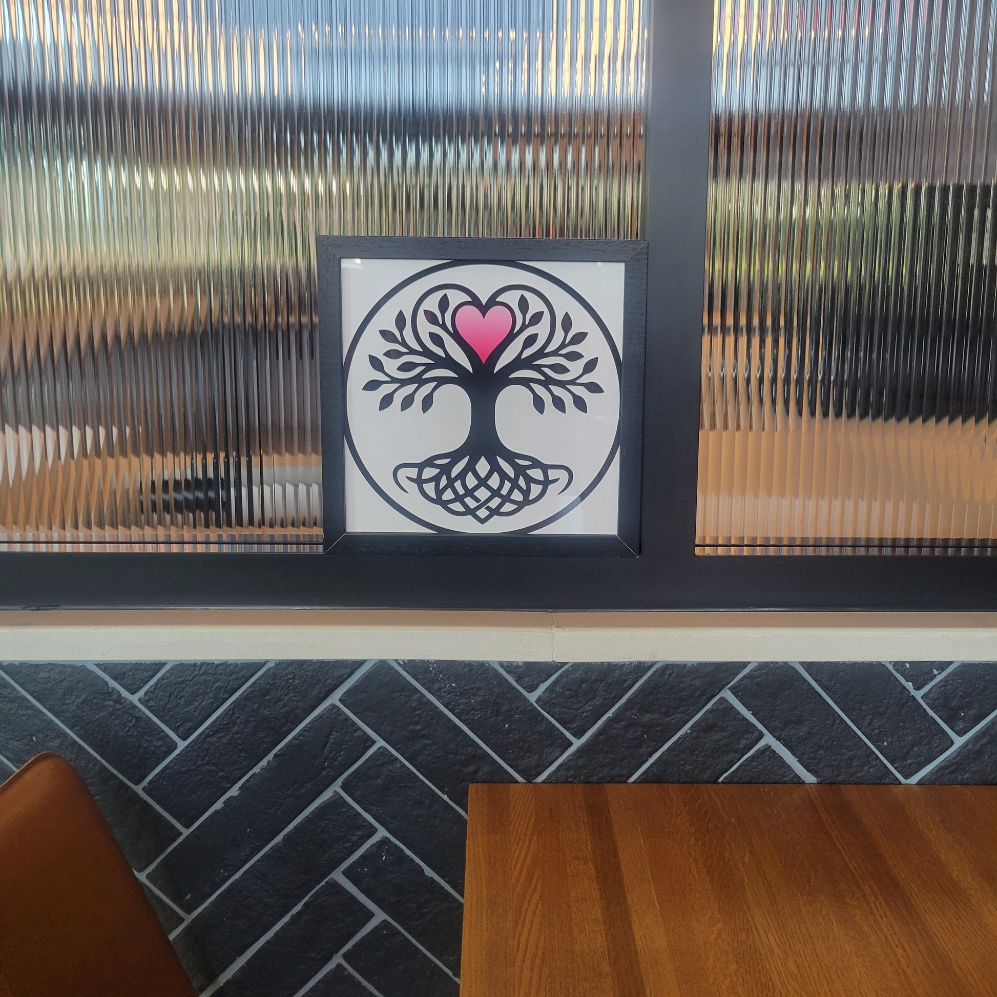 Black and white framed print of a Norse-style Tree of Life in a circle, with Celtic knotwork roots and a pink heart at the crown, displayed on a windowsill. Framed wall art.