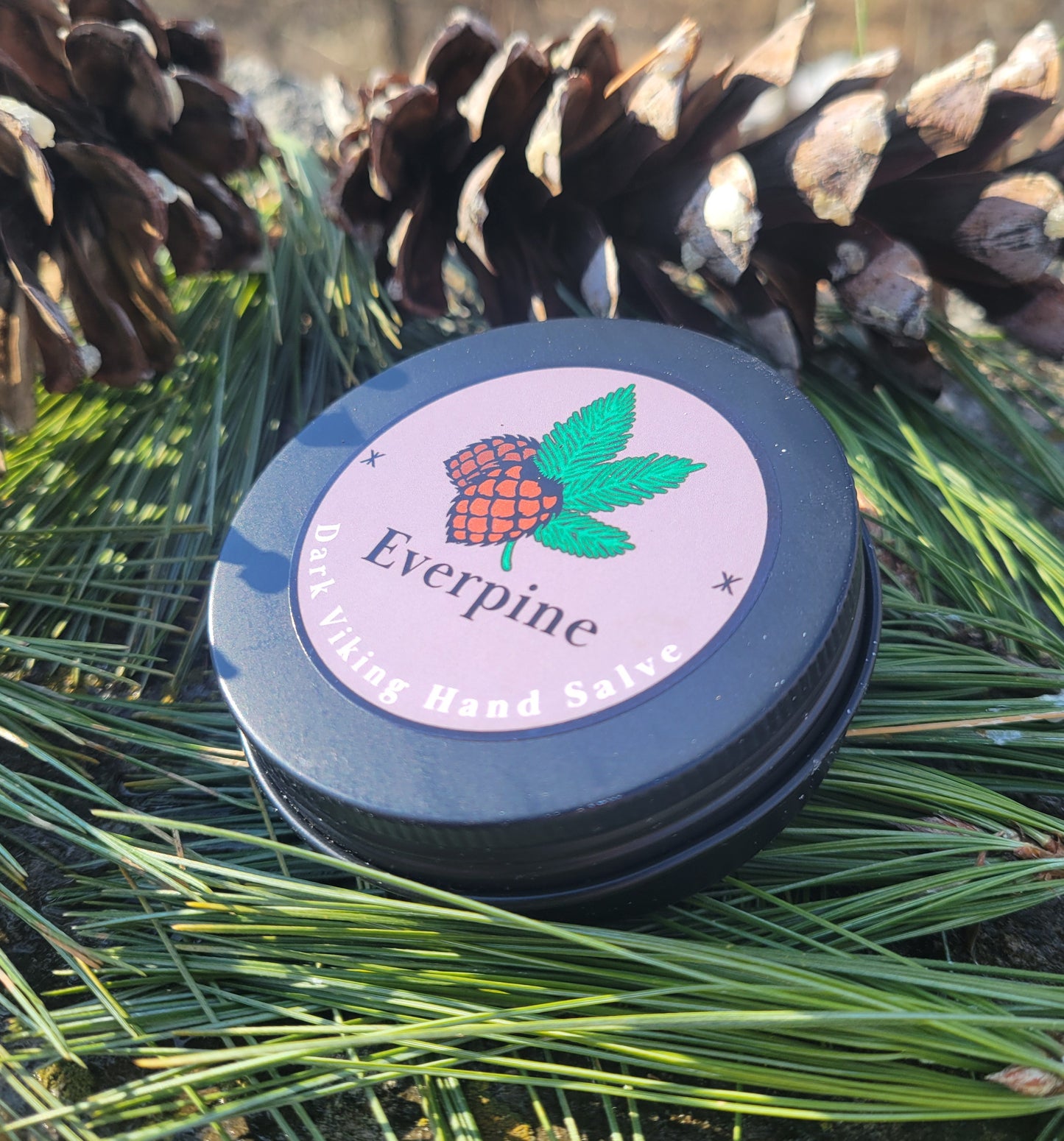 Hand salve container with 'Everpine' branding on a background of greenery and pine cones.