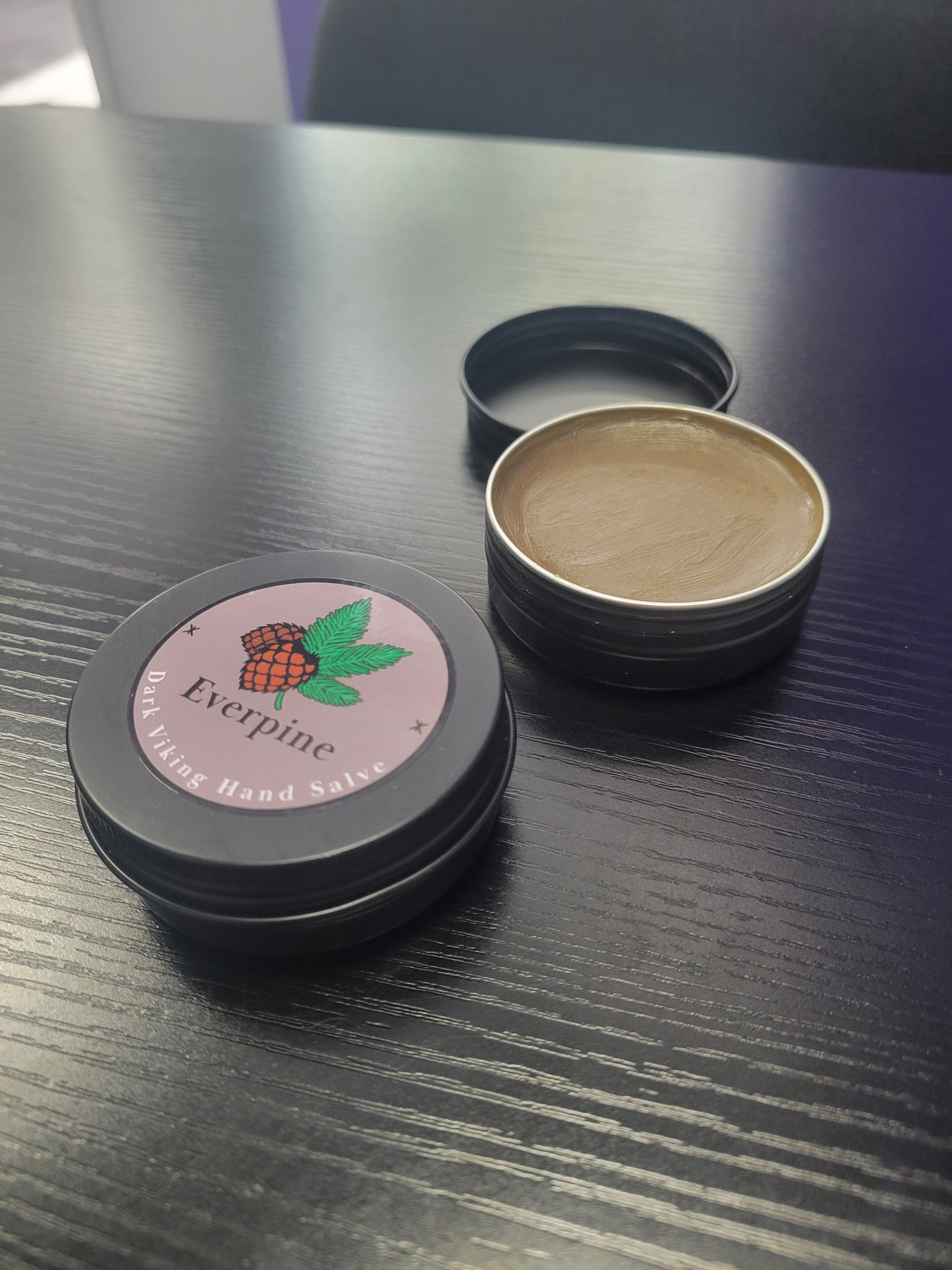 Black tin with a lid showing a brand logo on a metallic surface