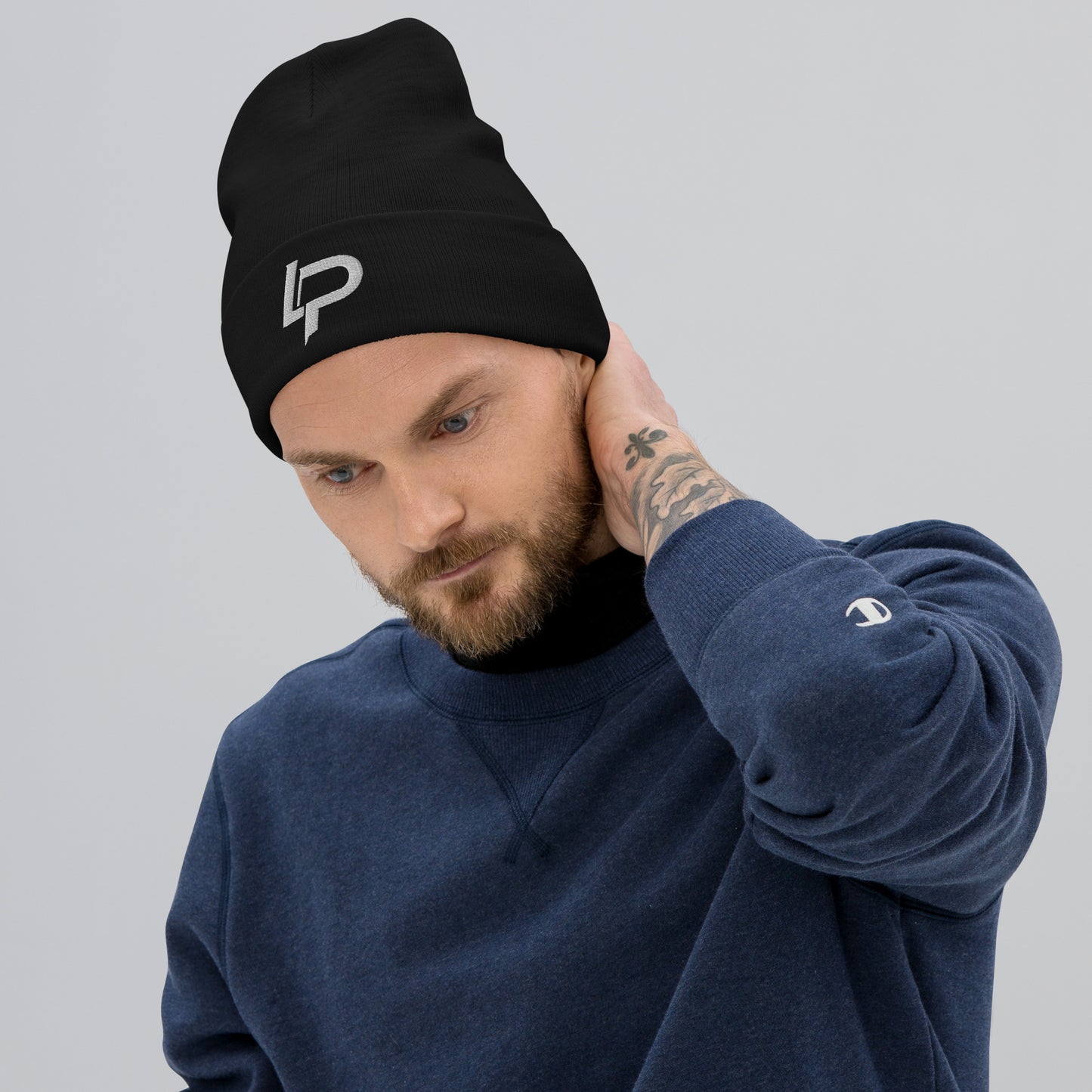 Bearded man wearing a black ribbed cuffed beanie with a white embroidered "LP" logo, paired with a navy Champion sweatshirt, against a light gray background. Embroidered beanie.