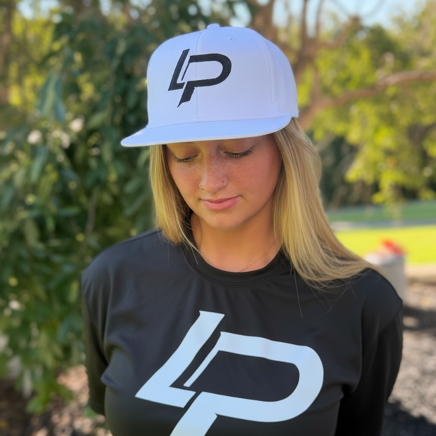 Blonde woman wearing a white snapback hat and black tee, both featuring a bold "LP" monogram logo, photographed outdoors; apparel lifestyle photo.