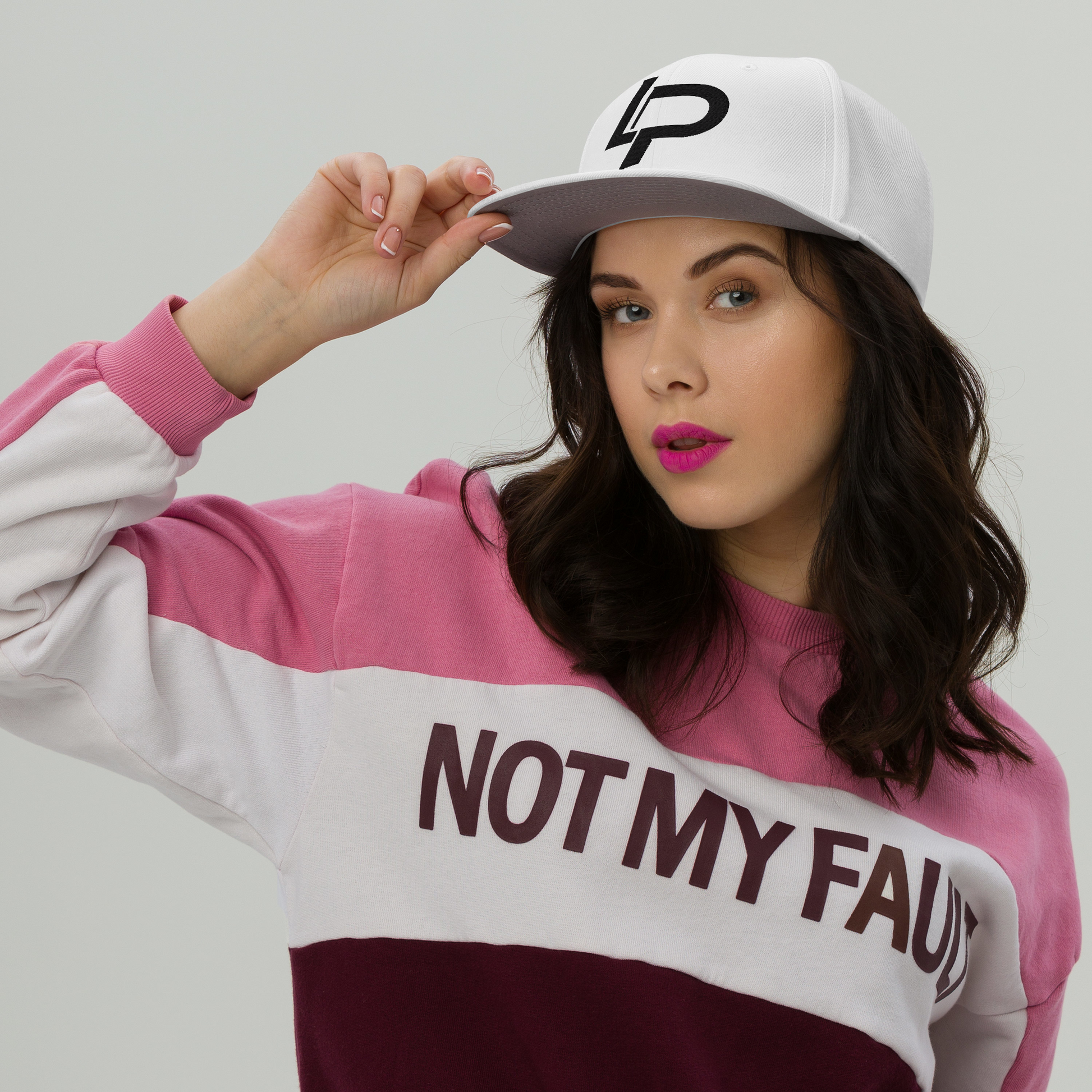 Dark-haired woman wearing a pink color-block sweatshirt and modeling a white snapback cap with black LP logo, apparel lifestyle photo.