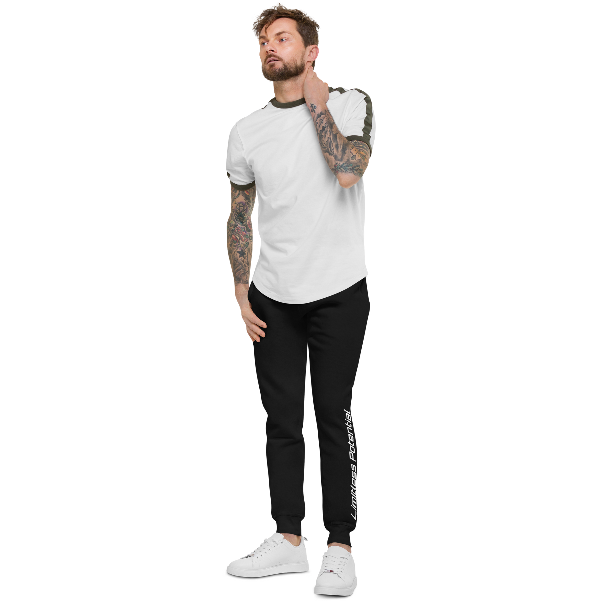 Tattooed male model wearing black joggers with "Limitless Potential" printed vertically on the left leg, paired with a white and olive tee — apparel lifestyle shot.