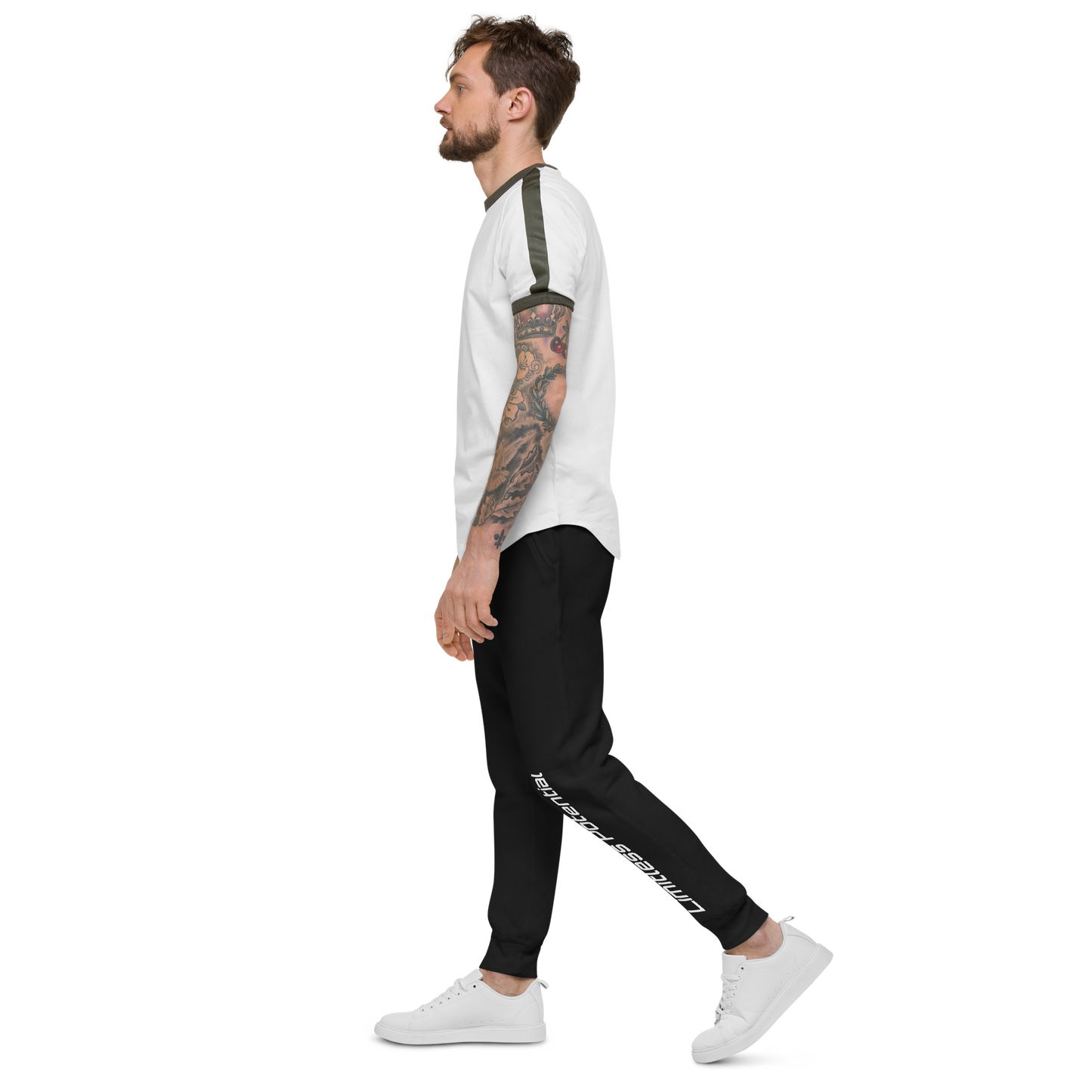Tattooed man in profile wearing white tee with olive trim and black joggers reading "Limitless Potential" along the left leg, apparel lifestyle shot.