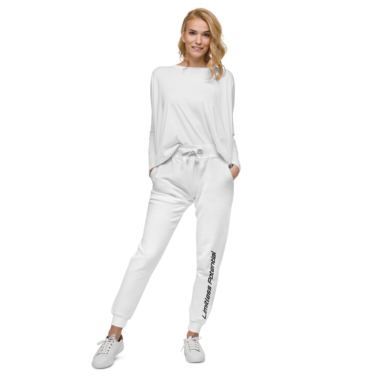 Woman wearing all-white jogger sweatpants with "Limitless Potential" printed vertically along the lower left leg, paired with a relaxed white long-sleeve top and white sneakers. Apparel.