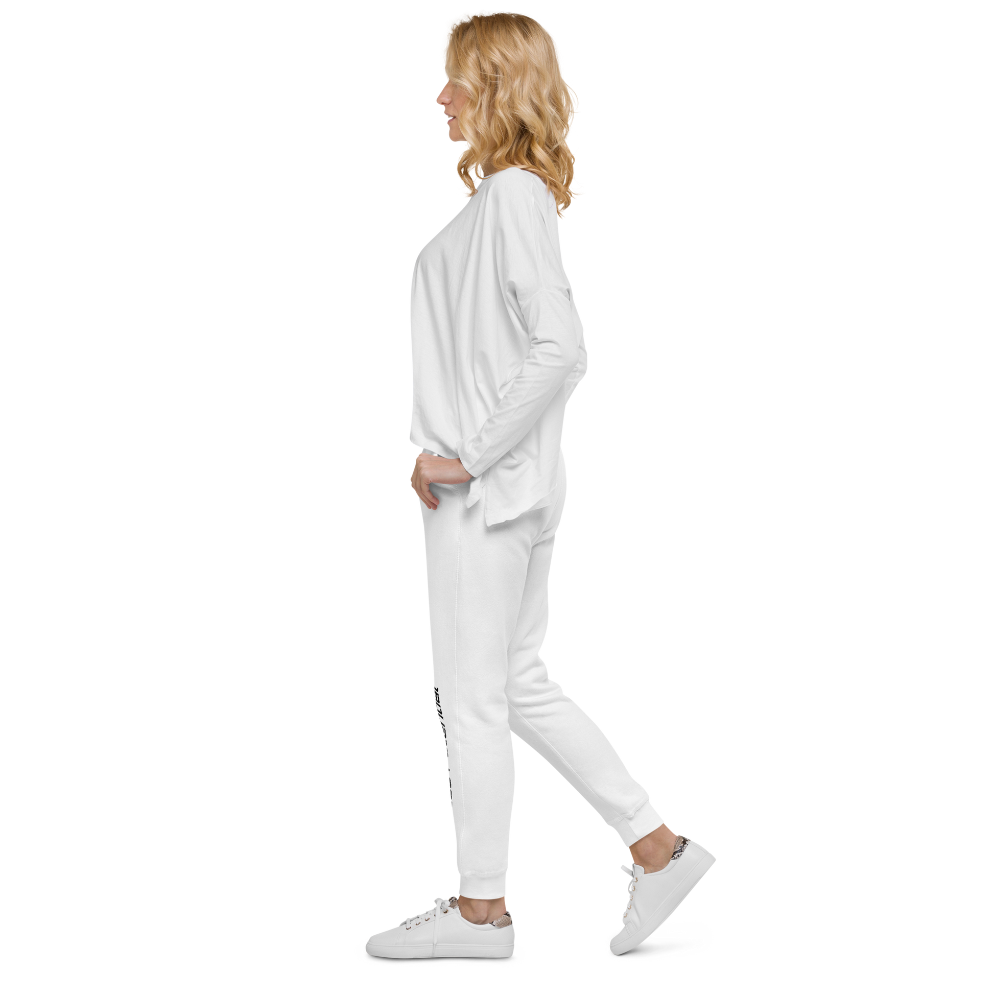 Woman modeling white jogger sweatpants with black "Limitless Potential" text along the lower left leg, paired with a white long-sleeve top, side view. Apparel.