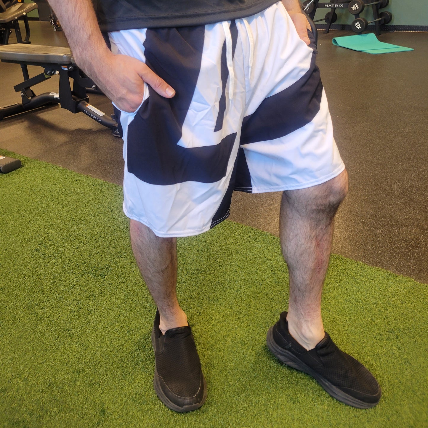 White athletic shorts with bold black LP graphic design worn by a model in a gym setting, shown from waist to feet, apparel.