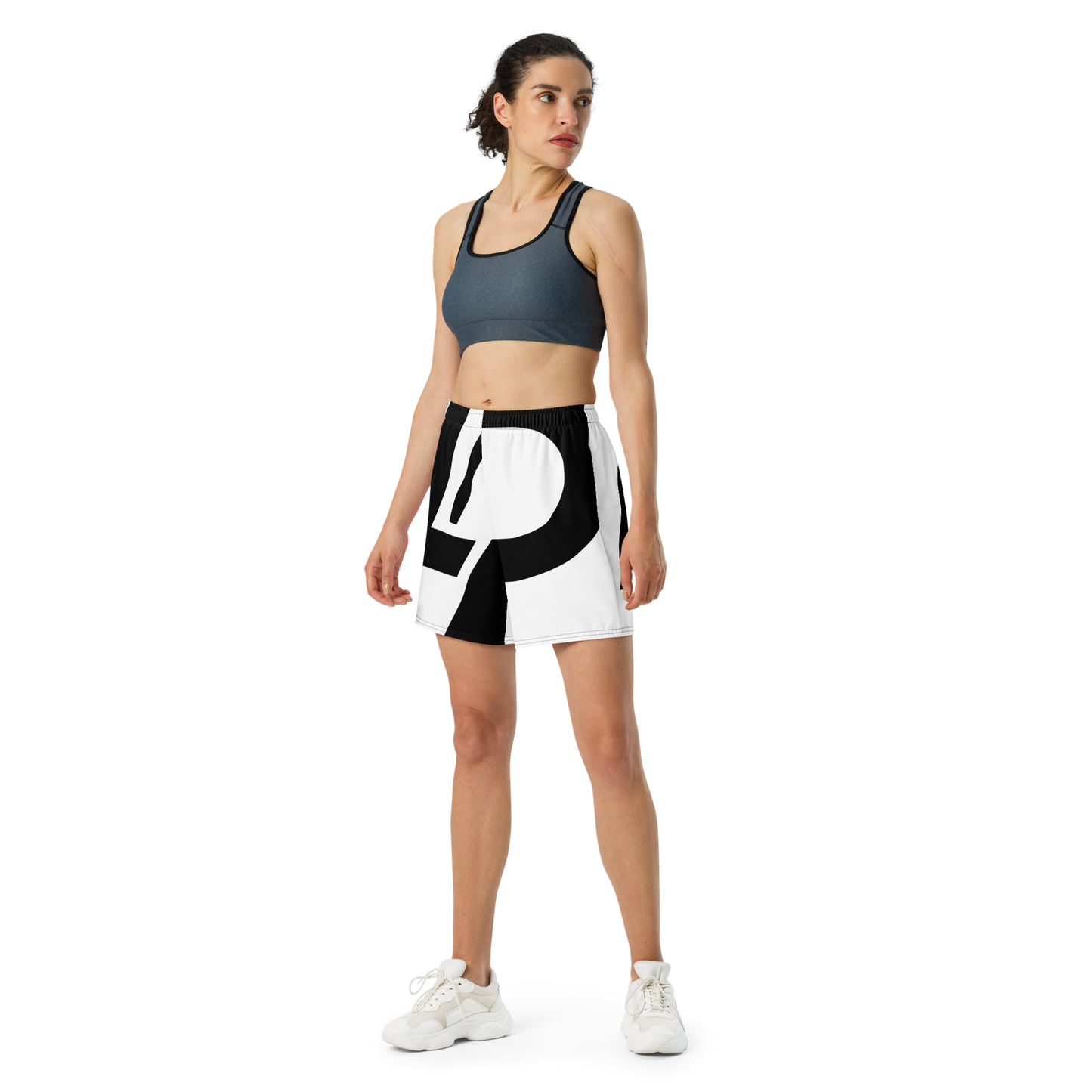 Woman wearing athletic shorts with black-and-white wraparound LP logo print, elastic waistband, paired with a slate sports bra and white sneakers.