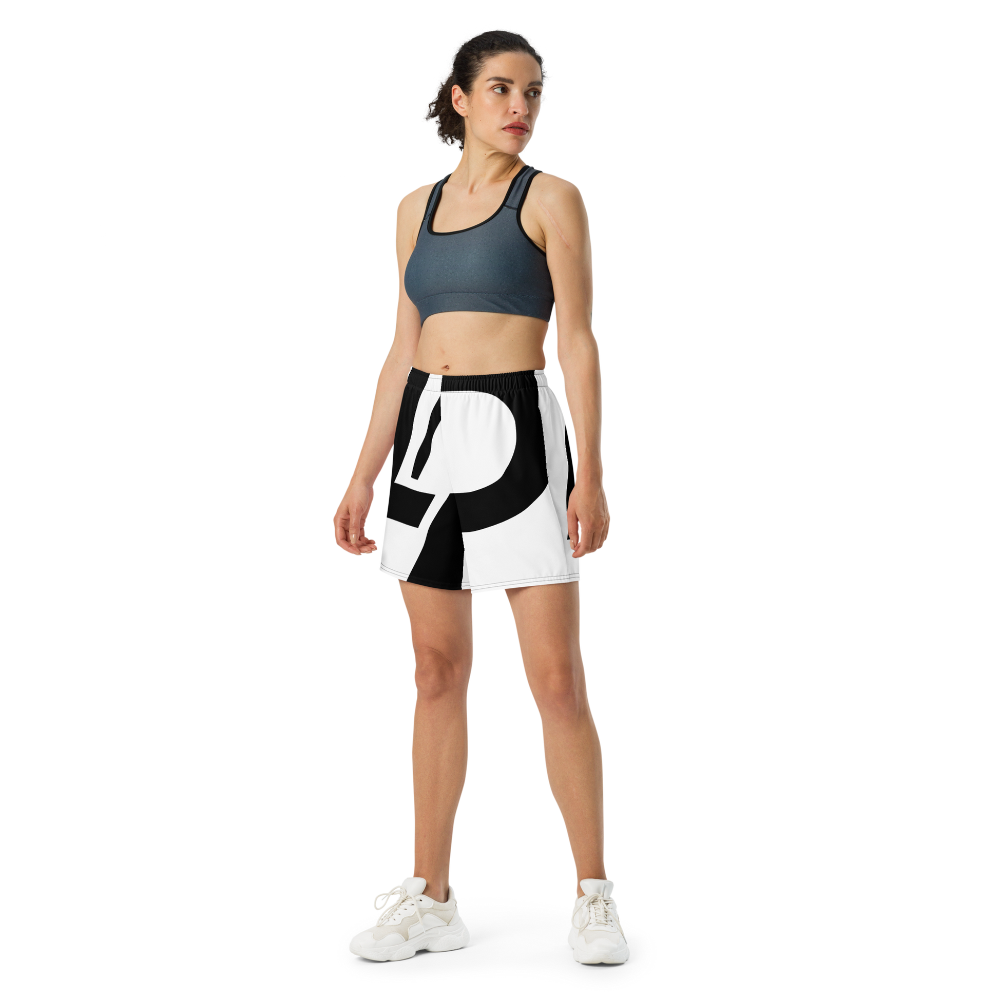 Woman wearing athletic shorts with black-and-white wraparound LP logo print, elastic waistband, paired with a slate sports bra and white sneakers.