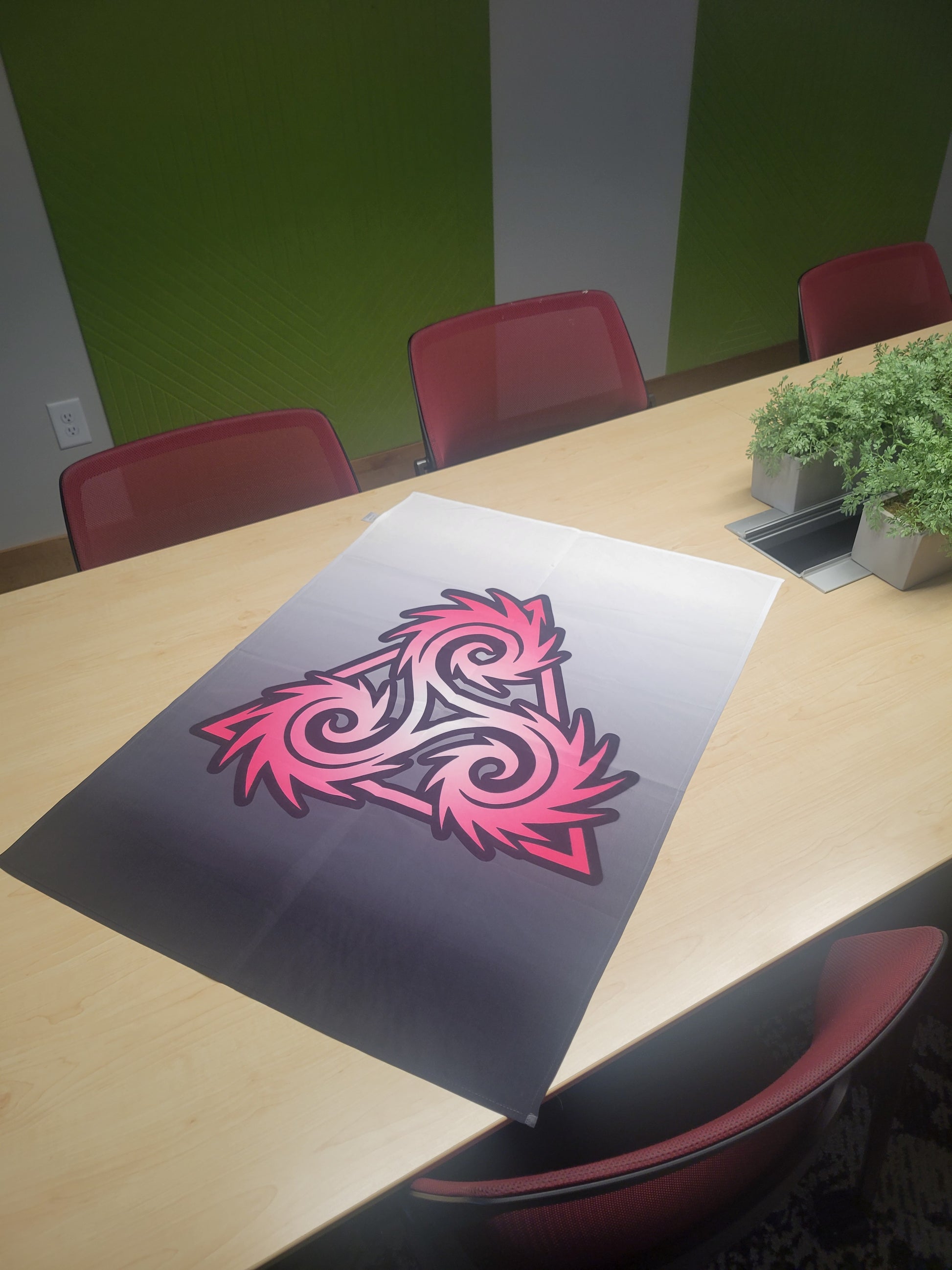Pink and black Triskelion symbol on a dark gradient background, displayed as a print on a conference table — wall art poster.