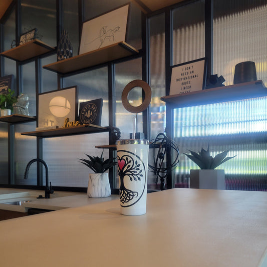 White insulated tumbler with a black and pink Yggdrasil tree-of-life design, displayed on a kitchen counter with industrial shelving in the background.