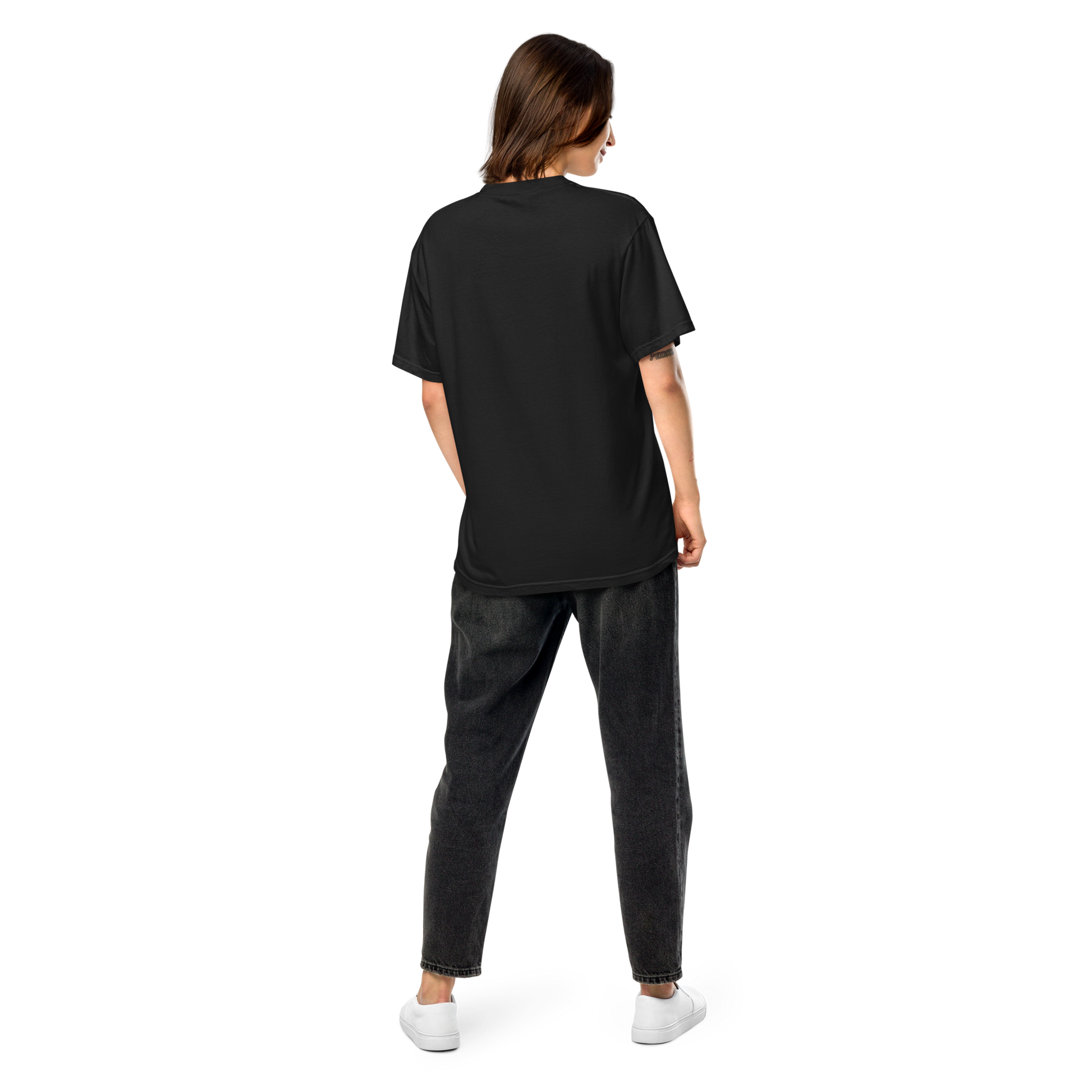 Back view of a model wearing a plain black oversized short-sleeve t-shirt with dark jeans and white sneakers, apparel.